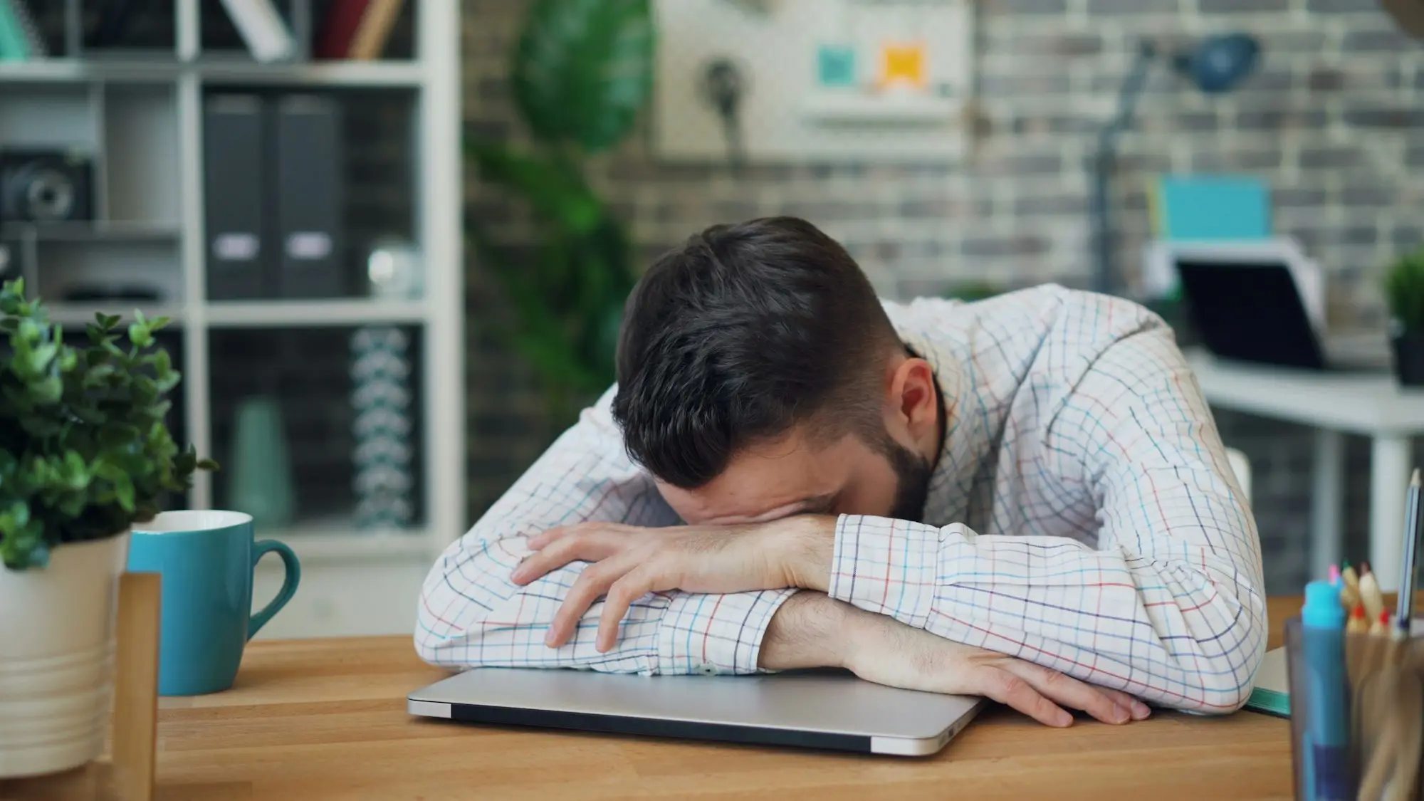 Business owner resting his head on his arms at a home office desk after learning he has been disqualified as a company director
